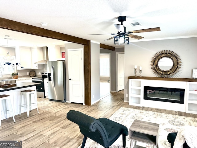 living room with sink, ceiling fan, beam ceiling, a textured ceiling, and light wood-type flooring