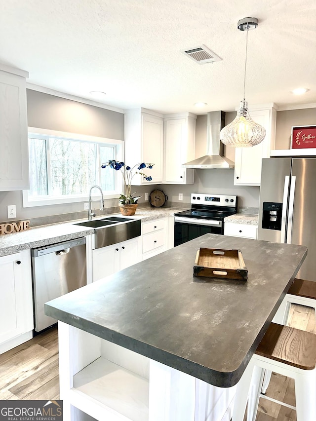 kitchen featuring appliances with stainless steel finishes, white cabinetry, sink, a center island, and wall chimney range hood