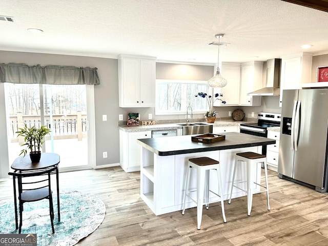 kitchen with wall chimney exhaust hood, appliances with stainless steel finishes, a center island, and white cabinets