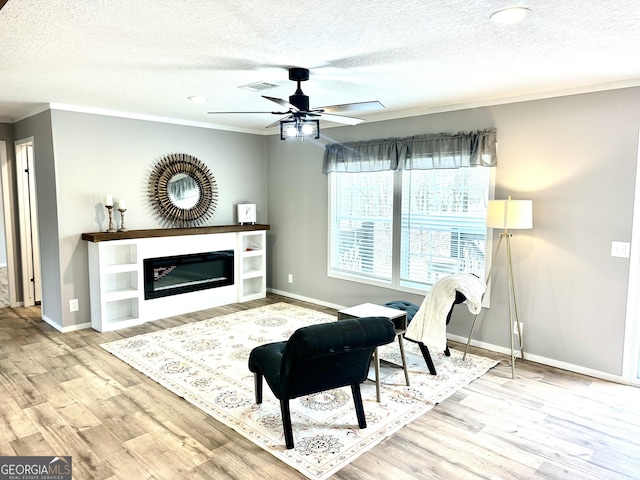 living room featuring ceiling fan, crown molding, light hardwood / wood-style floors, and a textured ceiling