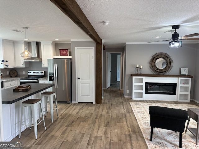 kitchen featuring white cabinetry, a kitchen breakfast bar, hanging light fixtures, stainless steel appliances, and wall chimney exhaust hood