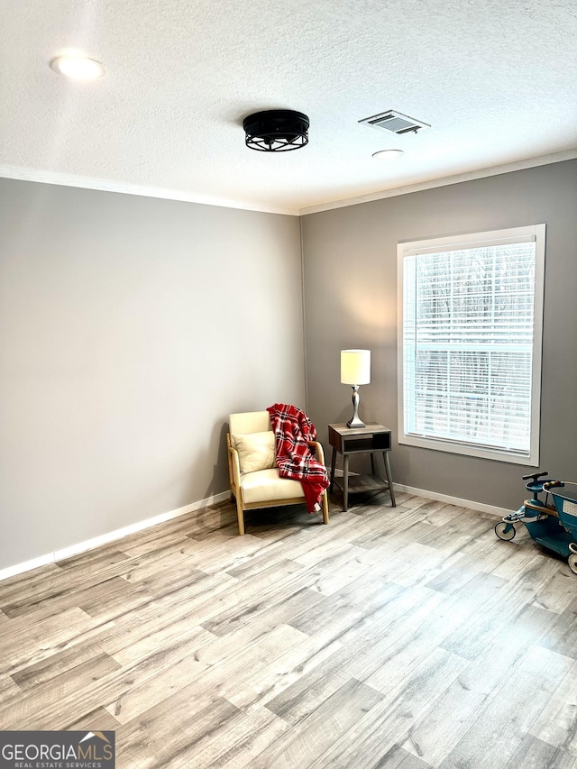 sitting room with crown molding, a textured ceiling, and light wood-type flooring