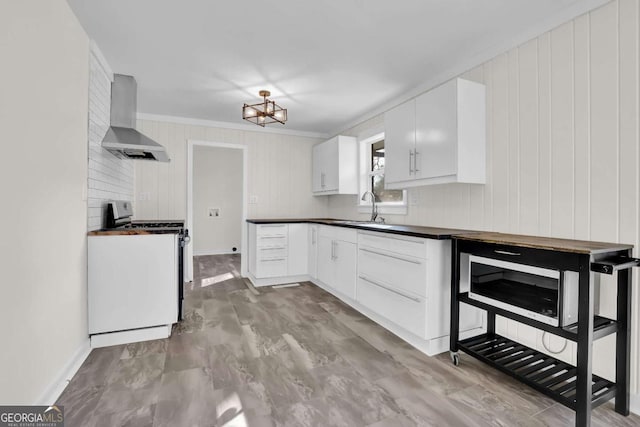 kitchen featuring stainless steel gas range, sink, ornamental molding, wall chimney range hood, and white cabinets