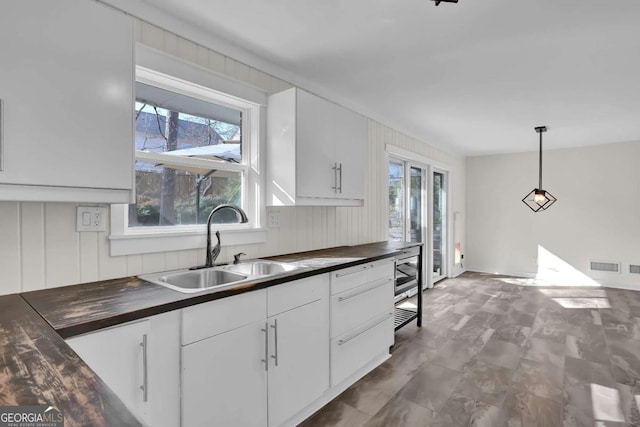 kitchen with stainless steel microwave, pendant lighting, sink, wooden counters, and white cabinets