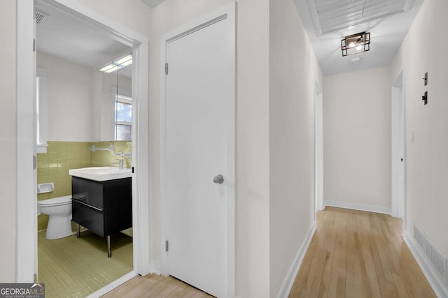 hall with sink, tile walls, and light hardwood / wood-style flooring