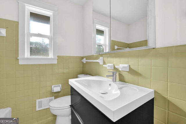 bathroom with a healthy amount of sunlight, toilet, vanity, and tile walls