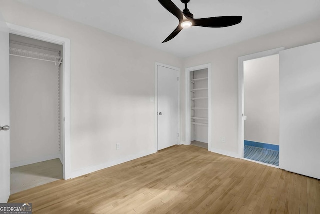 unfurnished bedroom featuring multiple closets, ceiling fan, and light wood-type flooring