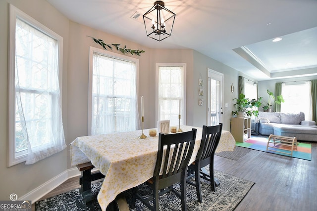 dining area with wood-type flooring, a raised ceiling, and a notable chandelier