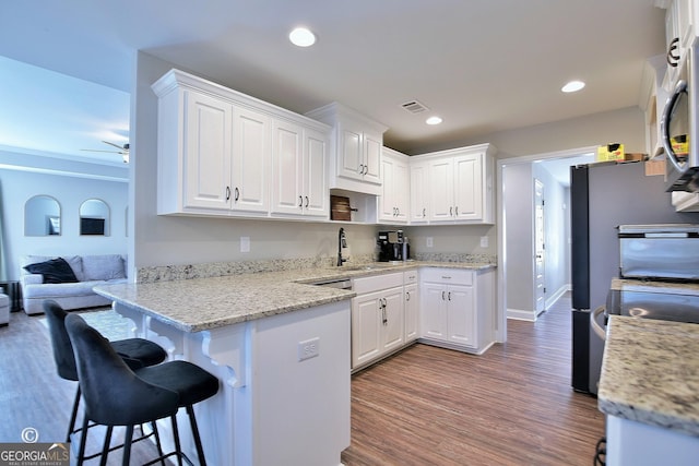 kitchen featuring sink, hardwood / wood-style flooring, white cabinetry, a kitchen breakfast bar, and light stone countertops