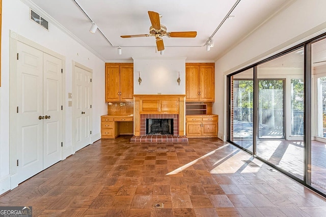 unfurnished living room with crown molding, a brick fireplace, track lighting, and ceiling fan