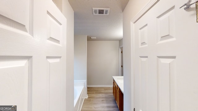 bathroom featuring hardwood / wood-style flooring, a tub to relax in, vanity, and a textured ceiling