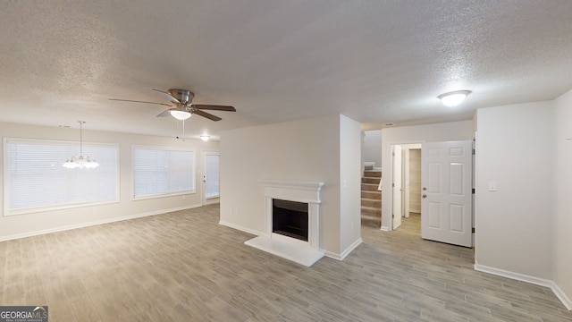 unfurnished living room with ceiling fan with notable chandelier, a textured ceiling, and light hardwood / wood-style flooring