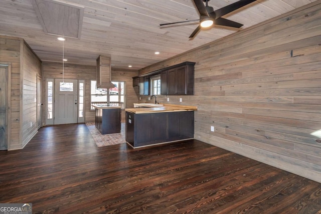 kitchen featuring dark wood-type flooring, dark brown cabinetry, wooden walls, and butcher block counters