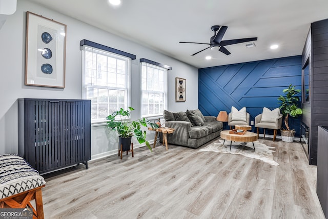 living room with ceiling fan, wooden walls, and light hardwood / wood-style flooring