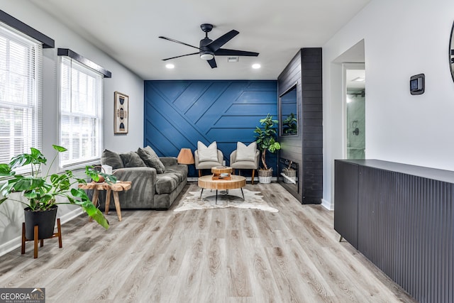 living room with wooden walls, ceiling fan, a fireplace, and light hardwood / wood-style flooring