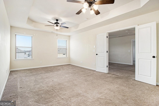 unfurnished bedroom featuring ceiling fan, light colored carpet, and a raised ceiling