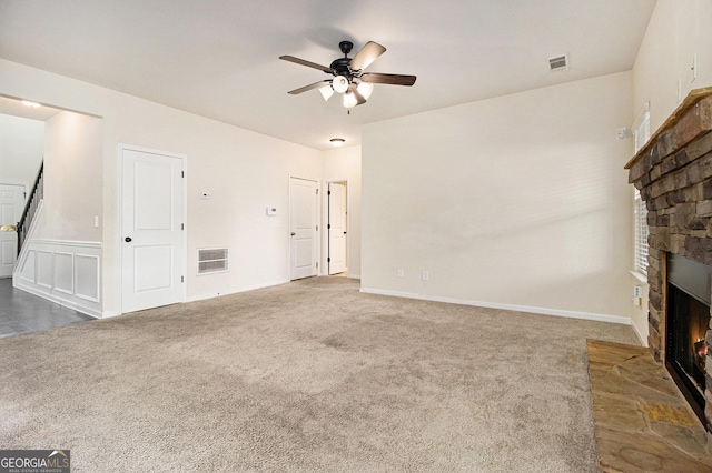 unfurnished living room featuring ceiling fan, a stone fireplace, and dark colored carpet