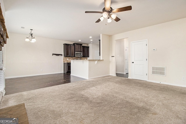 unfurnished living room with dark colored carpet and ceiling fan with notable chandelier