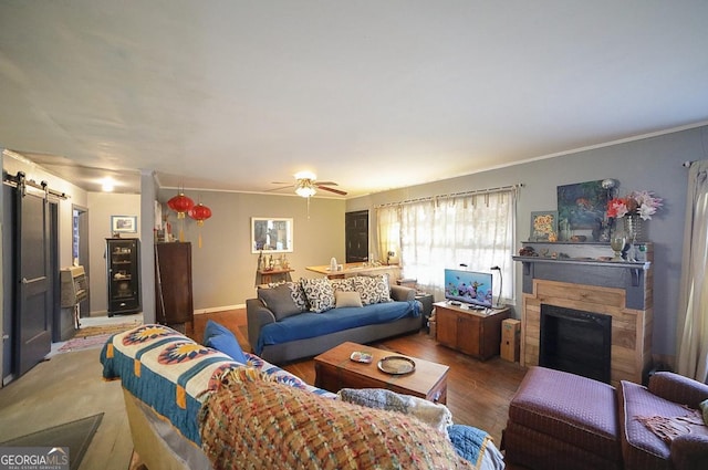 living room with wood-type flooring, a barn door, ceiling fan, and crown molding