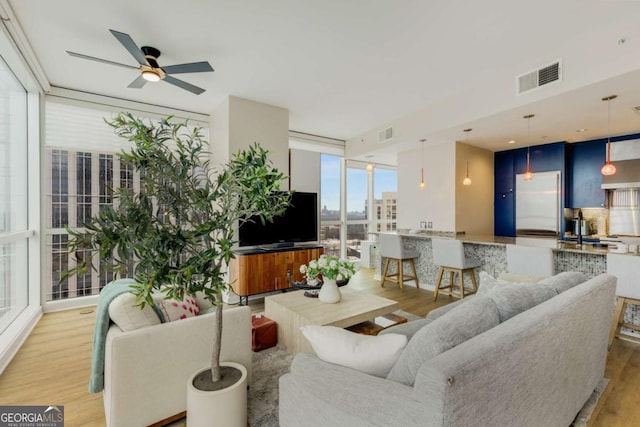living area featuring a wall of windows, ceiling fan, light wood finished floors, and visible vents