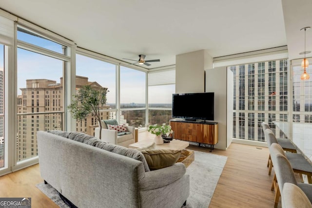 living area featuring ceiling fan, a healthy amount of sunlight, expansive windows, and light wood finished floors