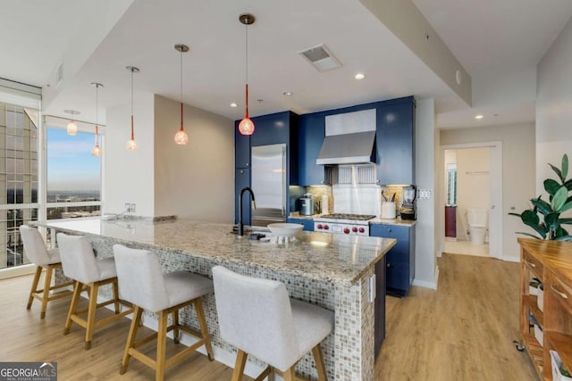 kitchen featuring a breakfast bar area, blue cabinets, visible vents, a sink, and light wood-style floors
