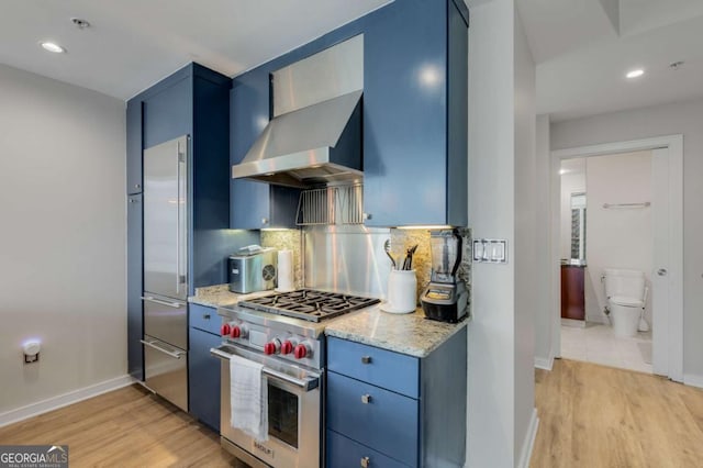 kitchen with premium appliances, light wood finished floors, wall chimney exhaust hood, and blue cabinets
