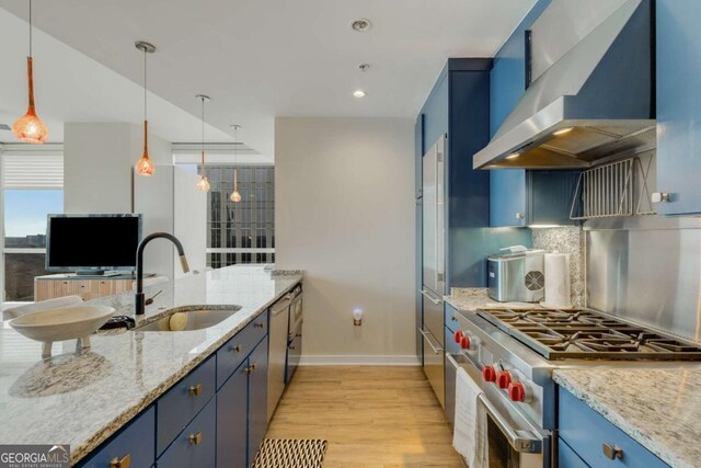 kitchen with wall chimney range hood, stainless steel appliances, a sink, and blue cabinets