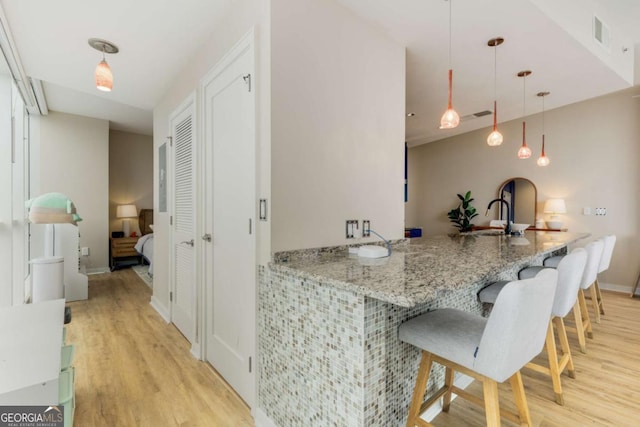 kitchen featuring a sink, a kitchen breakfast bar, a peninsula, decorative light fixtures, and light wood-type flooring