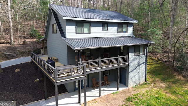 back of house featuring a patio area, a wooded view, and metal roof