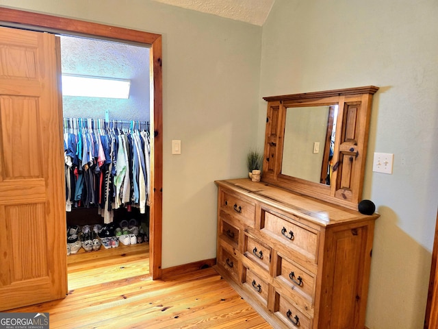 interior space featuring lofted ceiling, a textured ceiling, a closet, light wood-style floors, and baseboards