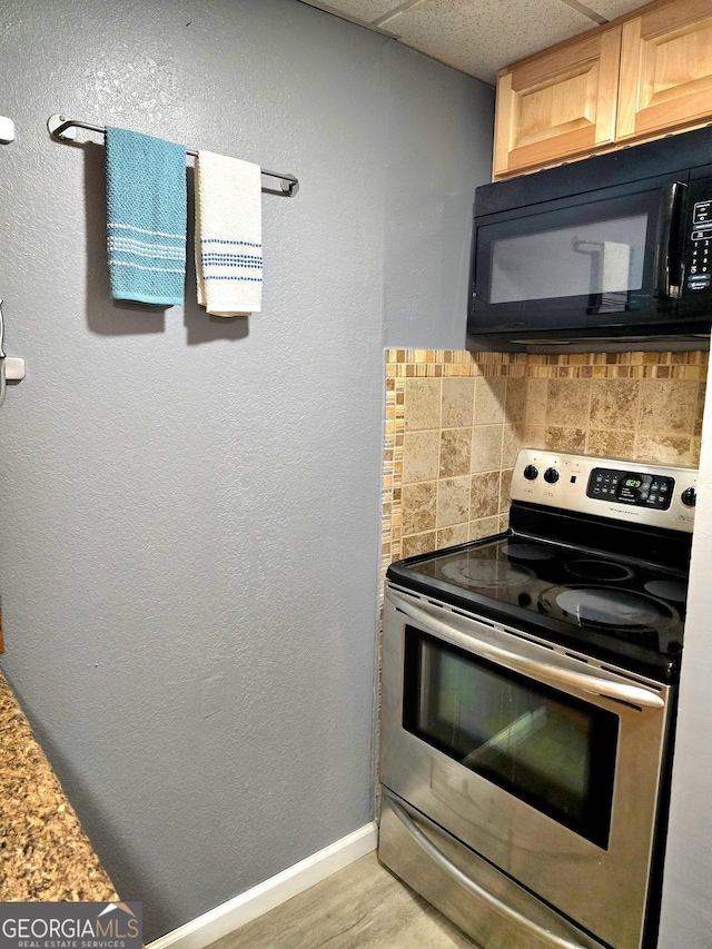 kitchen featuring stainless steel electric stove, baseboards, black microwave, decorative backsplash, and a paneled ceiling