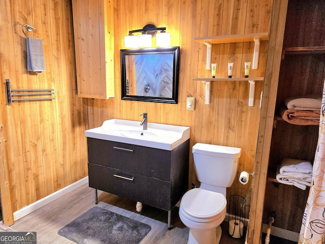 bathroom featuring wood walls, toilet, vanity, and wood finished floors