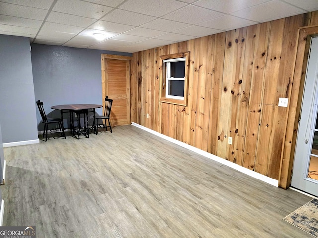 dining room with a drop ceiling, wood finished floors, baseboards, and wood walls