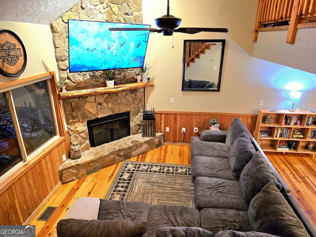 living room featuring wood finished floors, visible vents, a stone fireplace, wood walls, and wainscoting