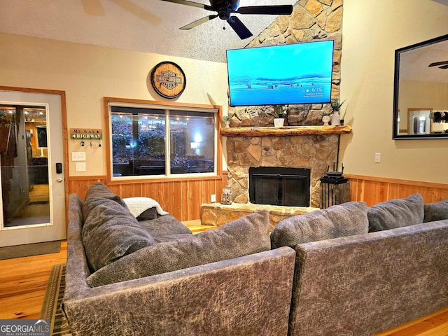 living area with a wainscoted wall, a ceiling fan, wood finished floors, wooden walls, and a fireplace