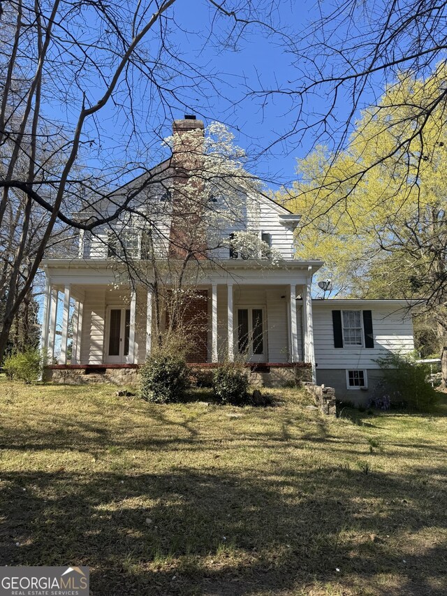view of front of property with a front lawn, french doors, a chimney, and covered porch