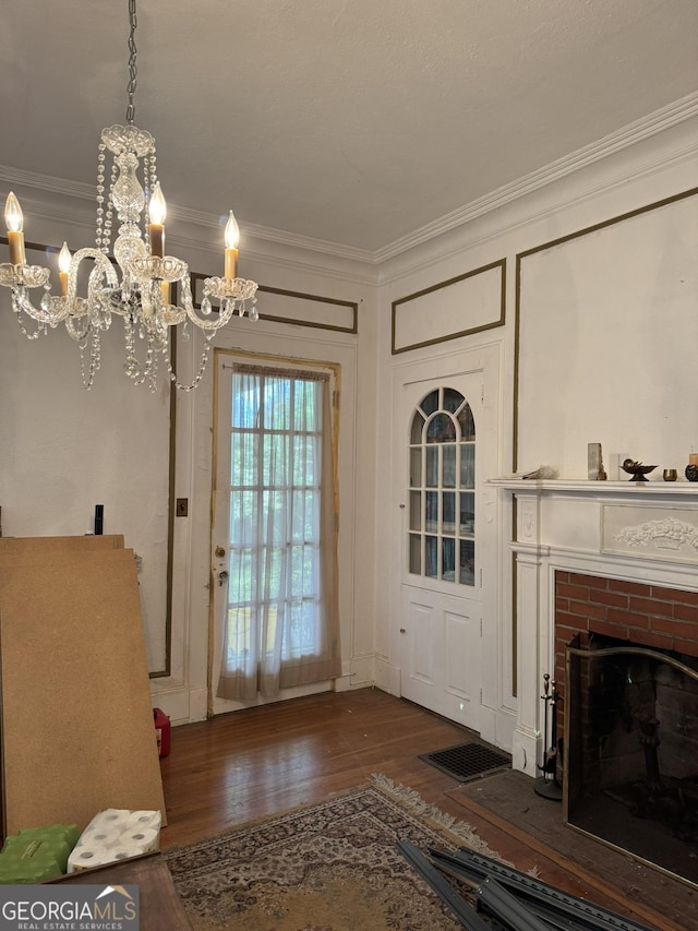 doorway to outside with ornamental molding, a brick fireplace, hardwood / wood-style floors, and a chandelier