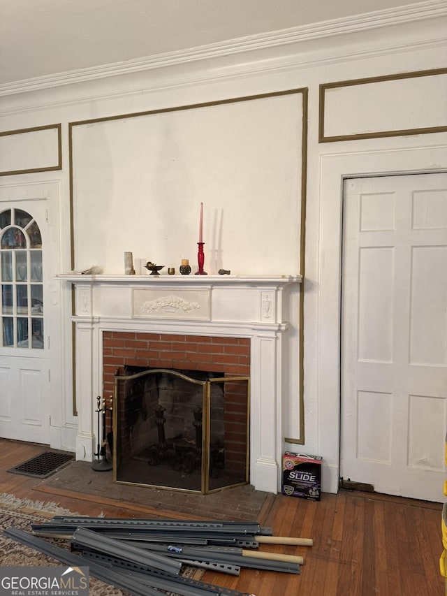 details featuring crown molding, visible vents, a decorative wall, wood finished floors, and a fireplace