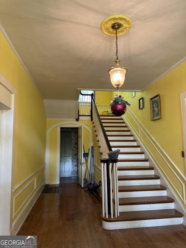 stairs with arched walkways, wainscoting, ornamental molding, a decorative wall, and hardwood / wood-style floors