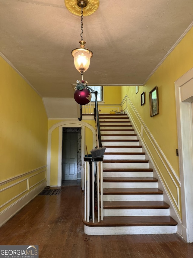 staircase featuring arched walkways, ornamental molding, and hardwood / wood-style flooring