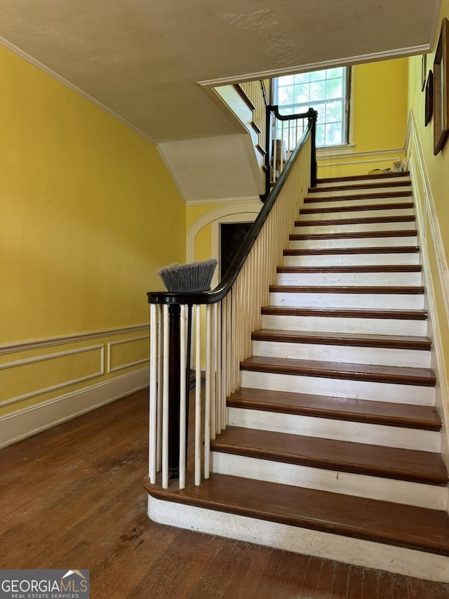 stairs with a wainscoted wall, ornamental molding, and hardwood / wood-style floors