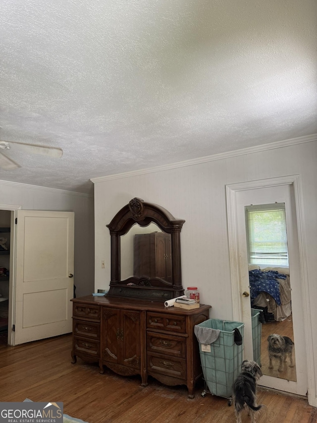 bedroom featuring a ceiling fan, a textured ceiling, ornamental molding, and wood finished floors
