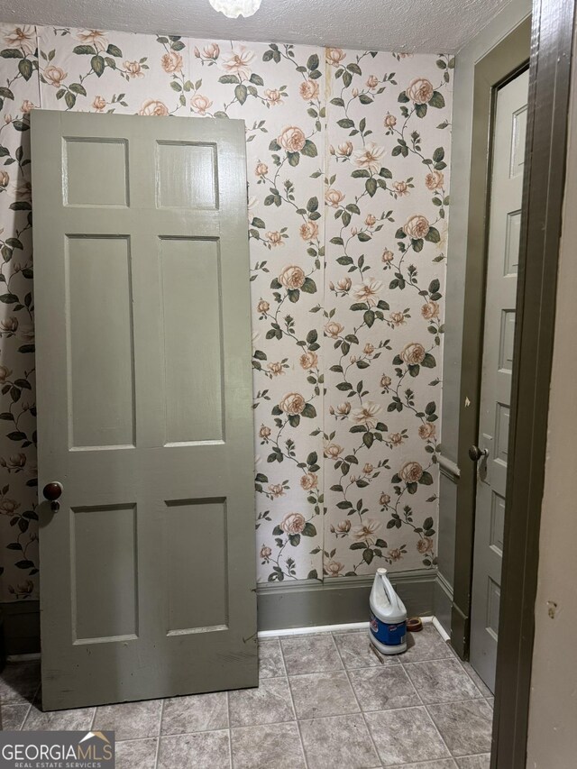 bathroom featuring a textured ceiling, wallpapered walls, and baseboards