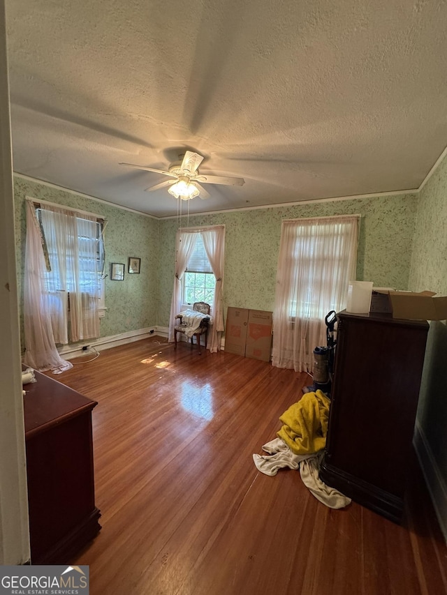 interior space featuring a ceiling fan, a textured ceiling, wood finished floors, and wallpapered walls