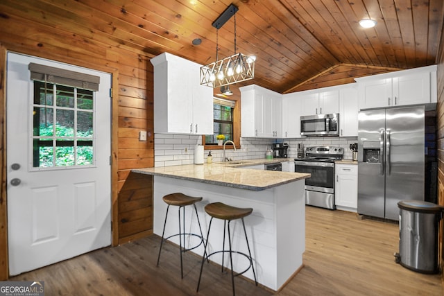 kitchen with light stone counters, appliances with stainless steel finishes, kitchen peninsula, pendant lighting, and white cabinets