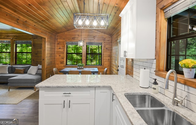 kitchen with white cabinetry, sink, light stone counters, and wooden walls