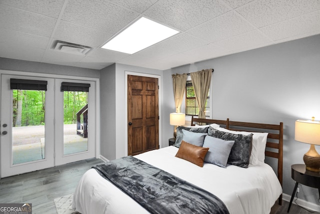 bedroom featuring french doors, a drop ceiling, hardwood / wood-style floors, and access to outside