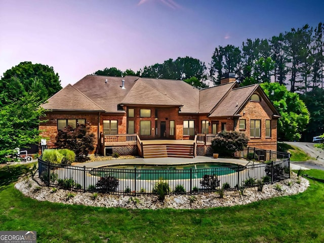 pool at dusk with a wooden deck and a yard