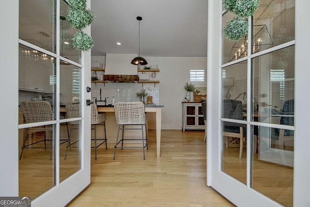 bar featuring light hardwood / wood-style flooring, decorative backsplash, custom exhaust hood, and french doors